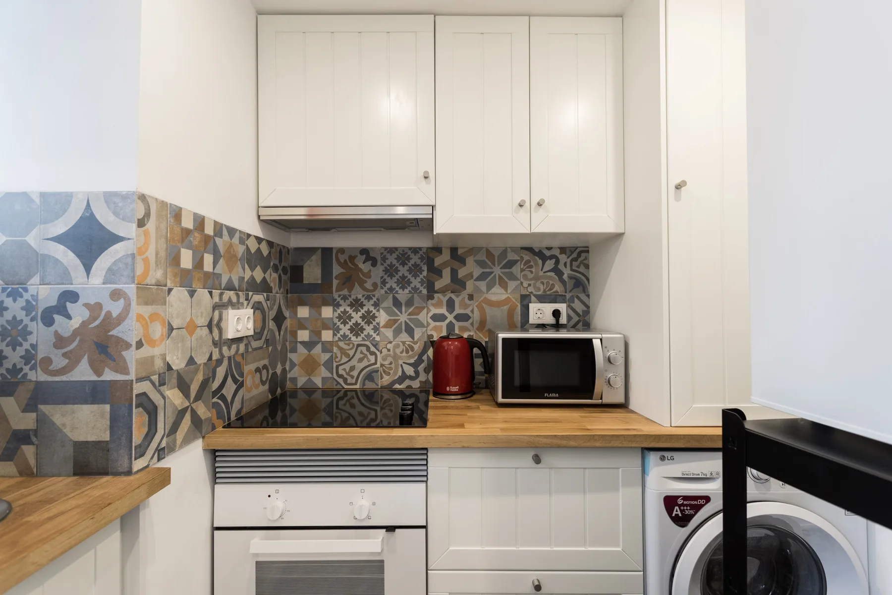 A compact kitchen with patterned tile backsplash and white cabinets.