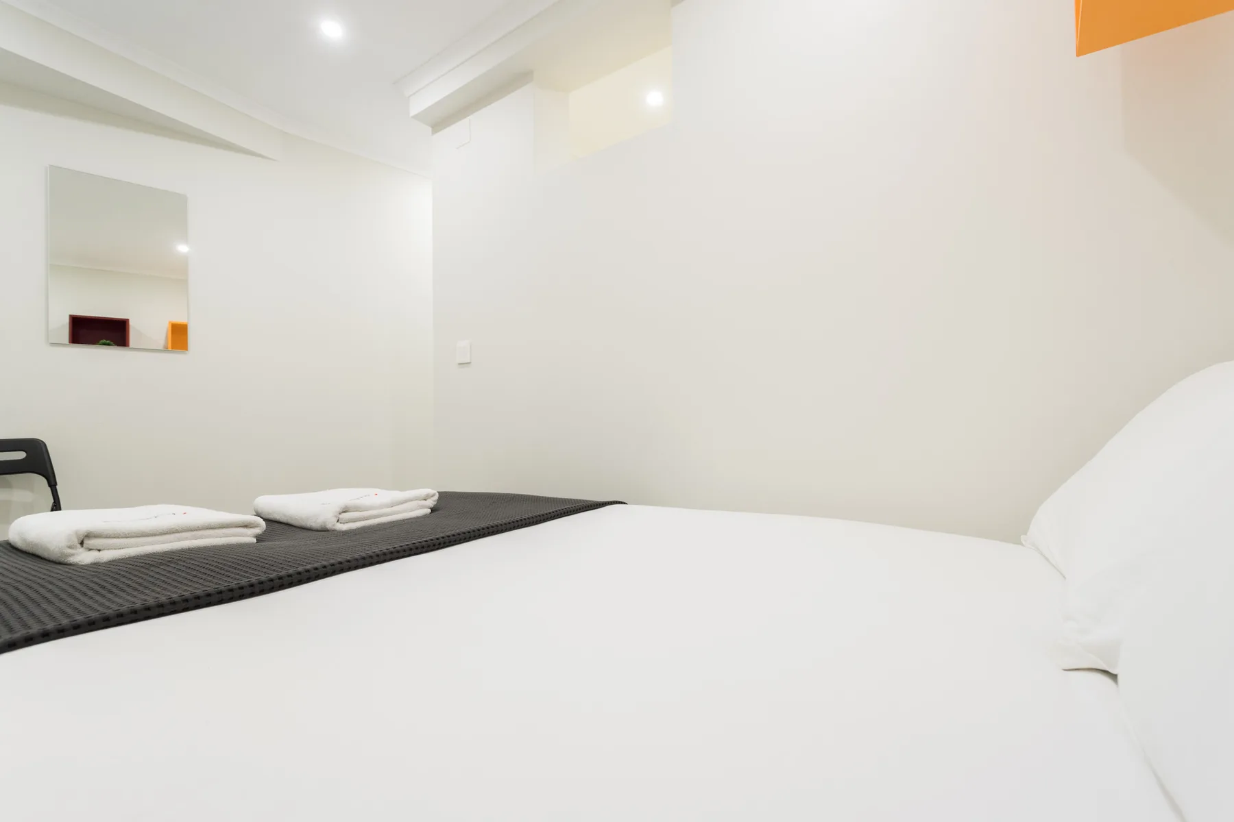 Un dormitorio luminoso con ropa de cama blanca y toallas dobladas sobre la cama.