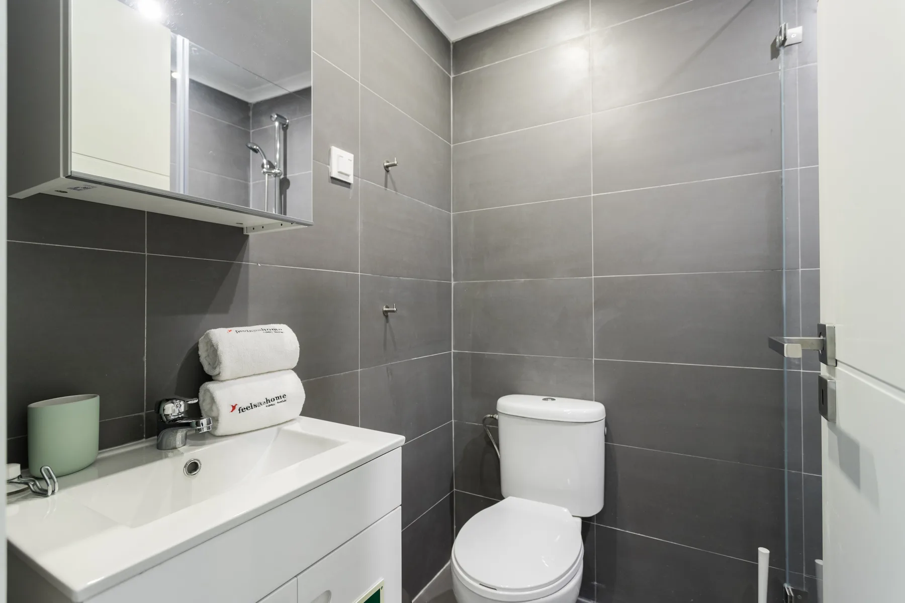 A bathroom with a sink, mirror, and toilet against gray tiled walls.