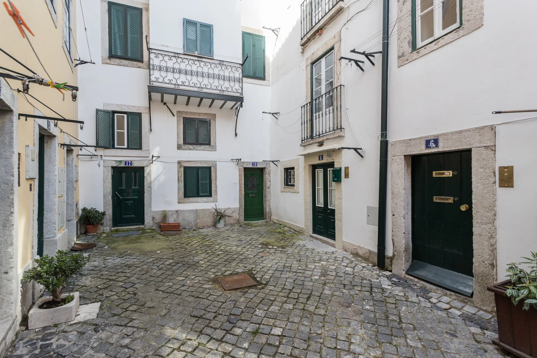 A small cobblestone courtyard is surrounded by white buildings with green doors and windows.
