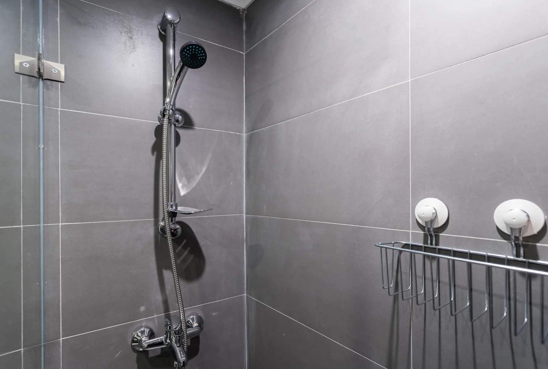 A tiled shower area with a handheld showerhead and wall-mounted controls.
