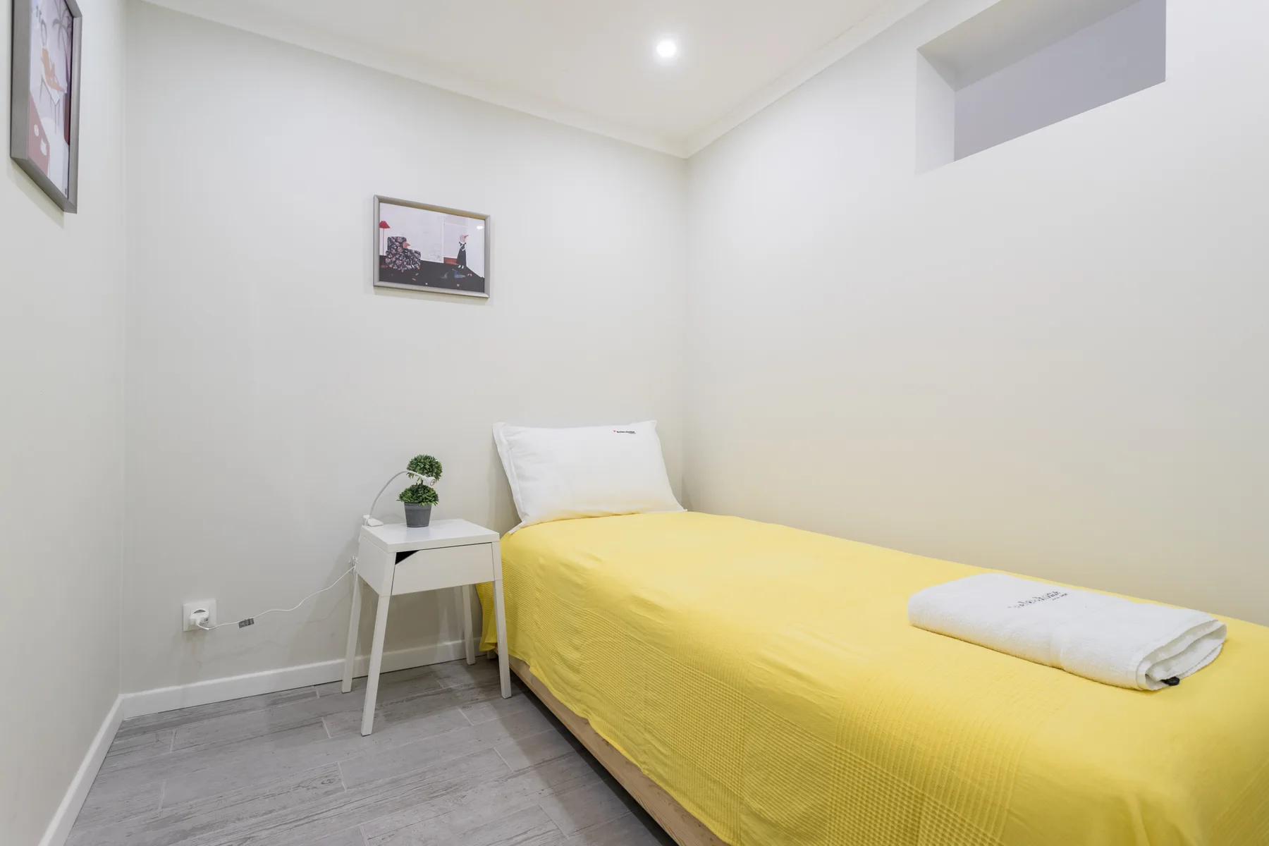 A bedroom with a bed covered in a bright yellow bedspread and a small bedside table.