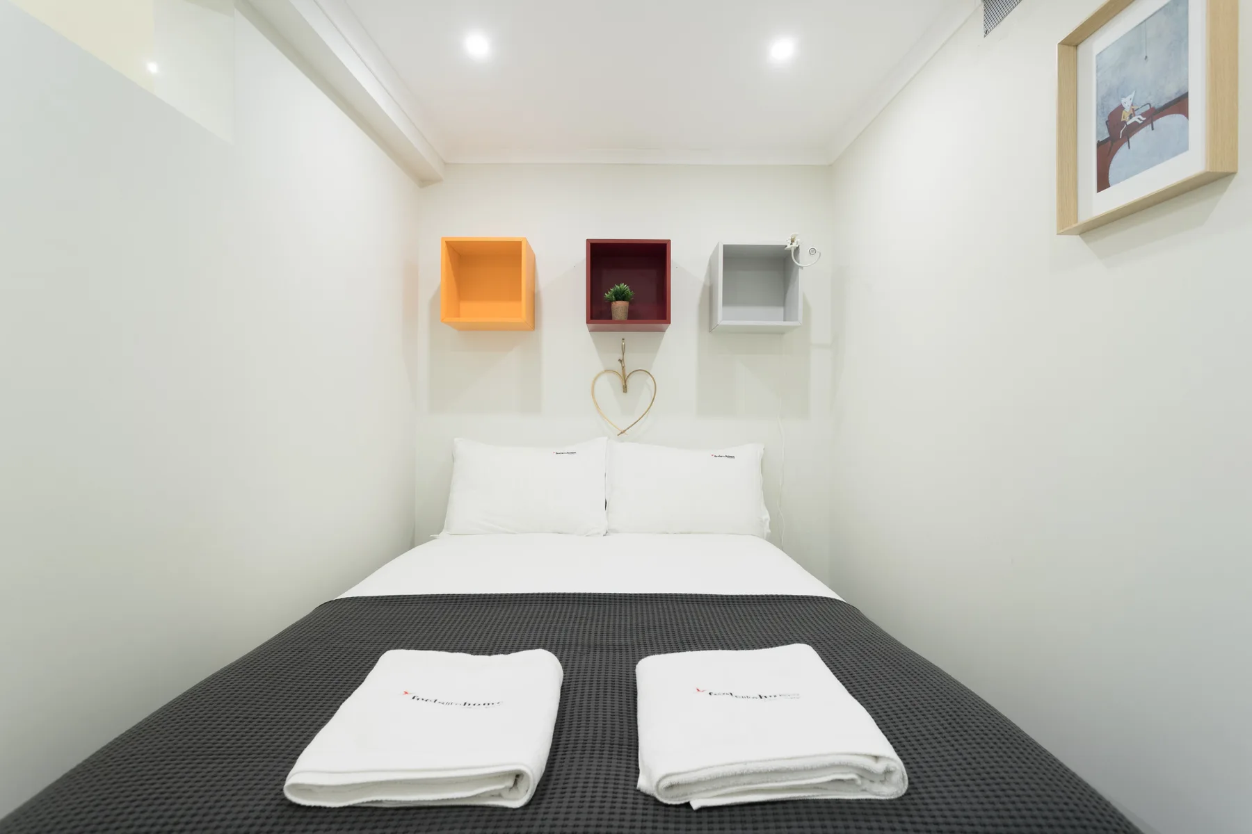 Un dormitorio con una cama bien tendida y tres estantes de colores en la pared.