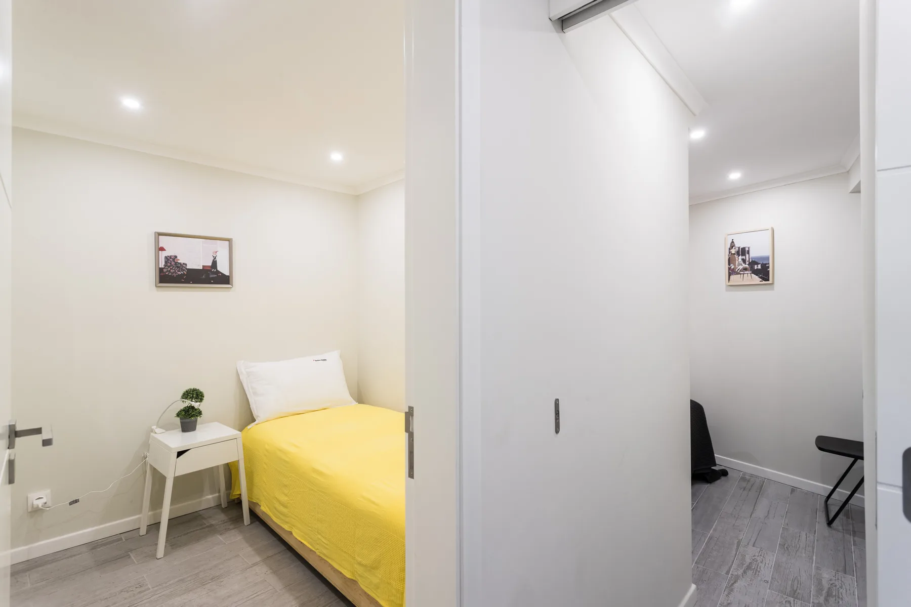A bright bedroom with a single bed, bedside table, and framed wall art.