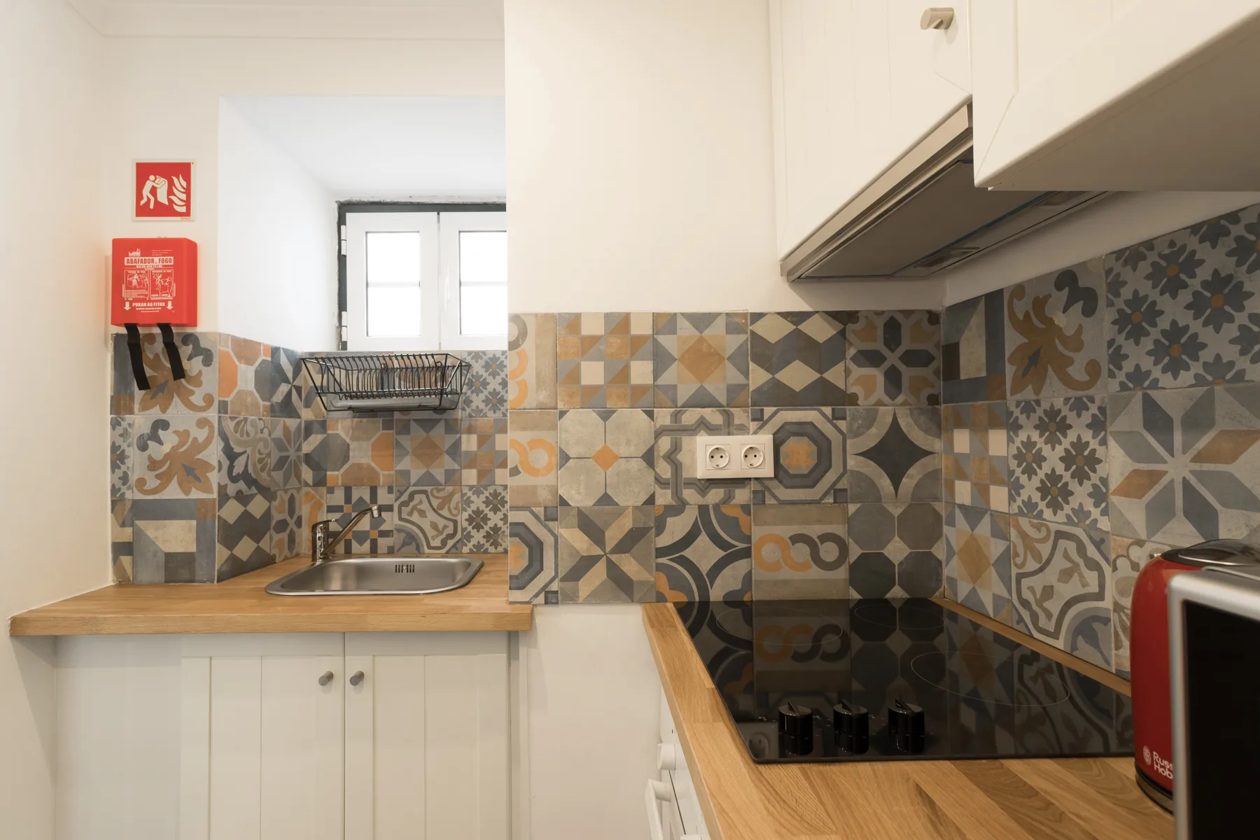 Una cocina compacta con encimeras de madera, azulejos estampados y una placa de cocina.