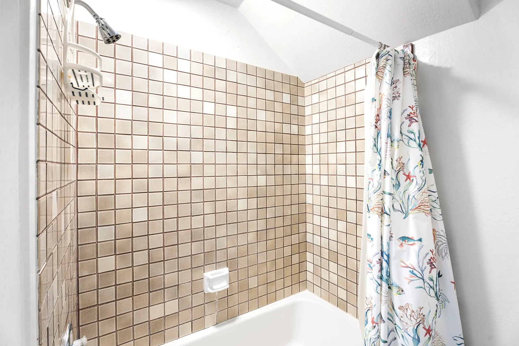 A tiled bathroom shower area with a patterned curtain beside the tub.