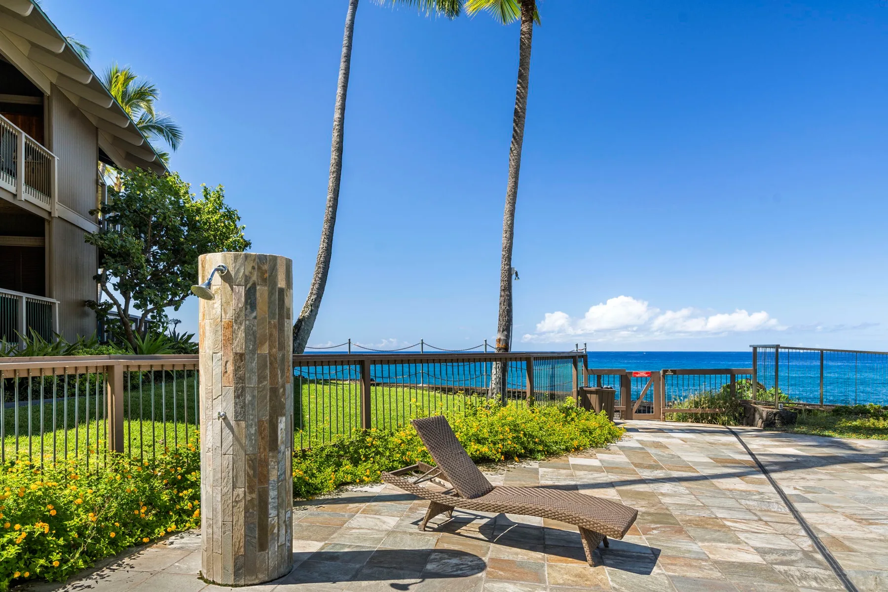 A tiled oceanfront patio has lounge seating beside a railing and outdoor shower.