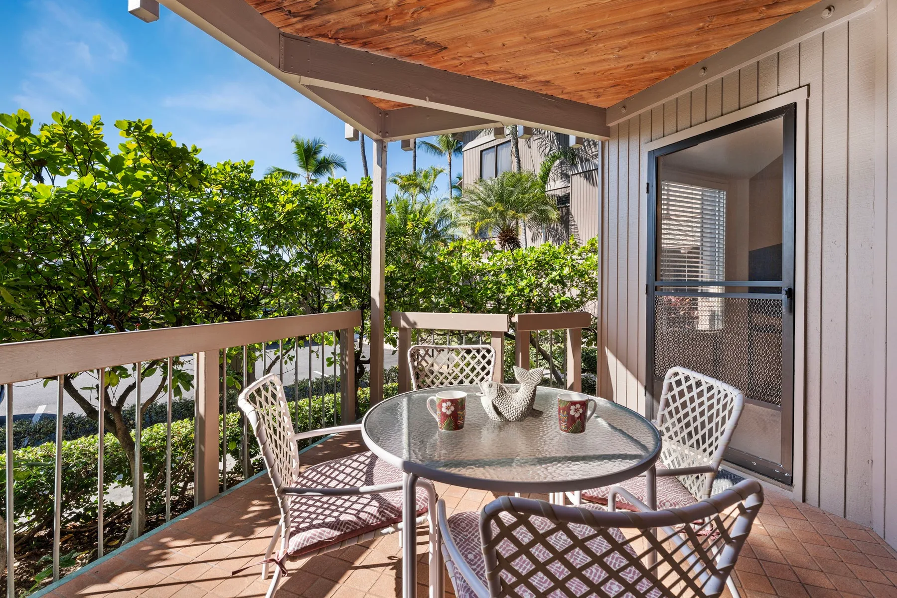 A covered patio with outdoor seating and a round table overlooks leafy trees.