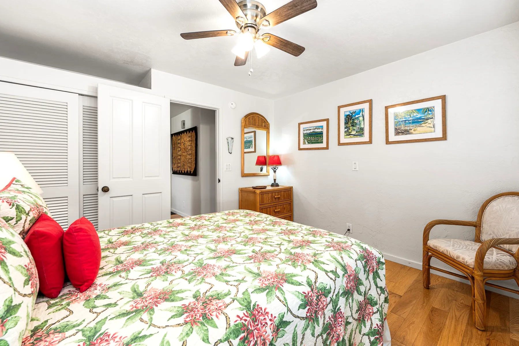 A bedroom with a floral bedspread, a ceiling fan, and framed pictures on the wall.