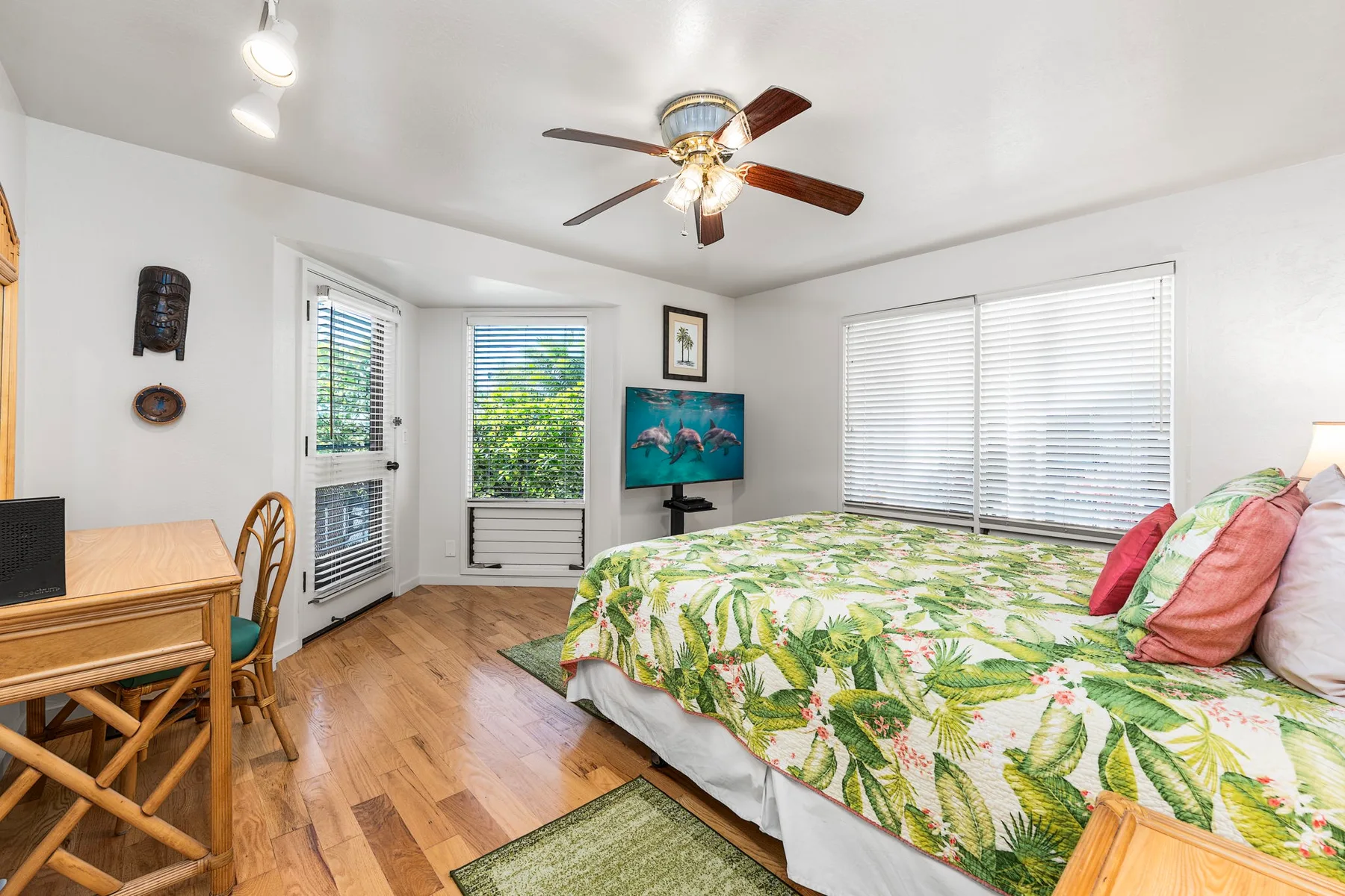 A bright bedroom with a leafy-patterned bedspread and a ceiling fan.