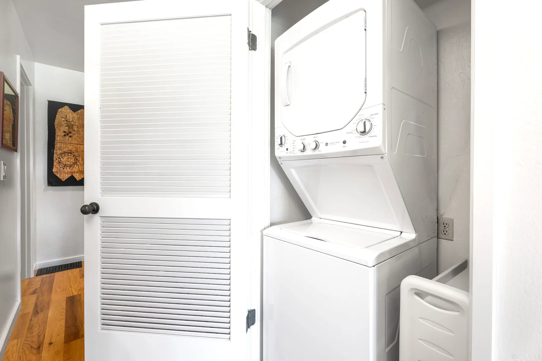 A laundry area with a stacked washer and dryer behind a louvered door.