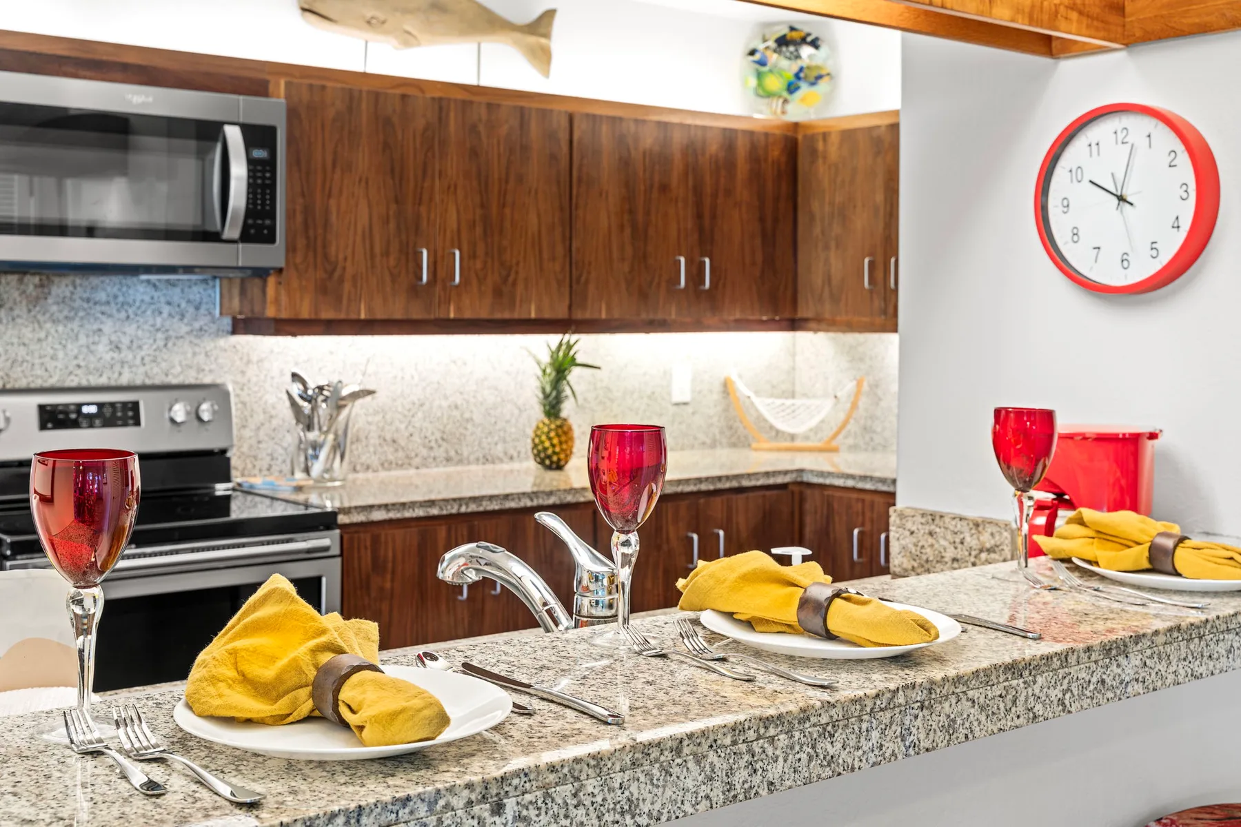 A kitchen with a granite island set with plates, napkins, and glasses.