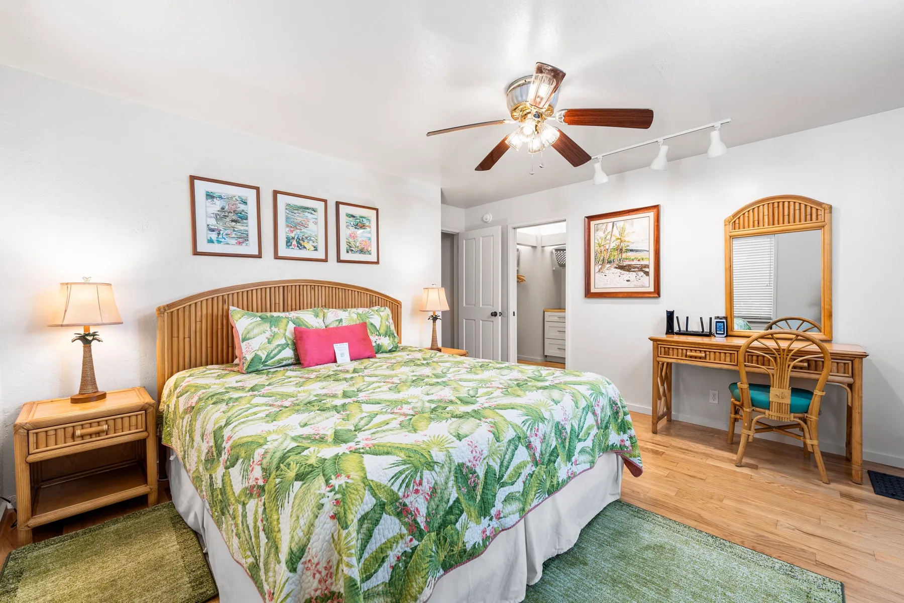 A bedroom with a bed covered in a leafy floral bedspread and a desk.