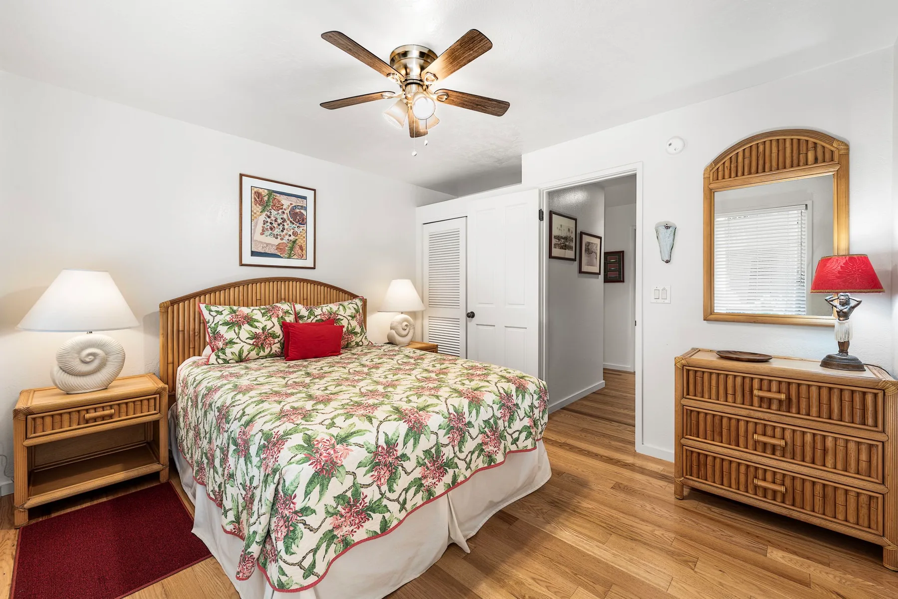 A bedroom with a floral bedspread, bedside tables, and a ceiling fan.