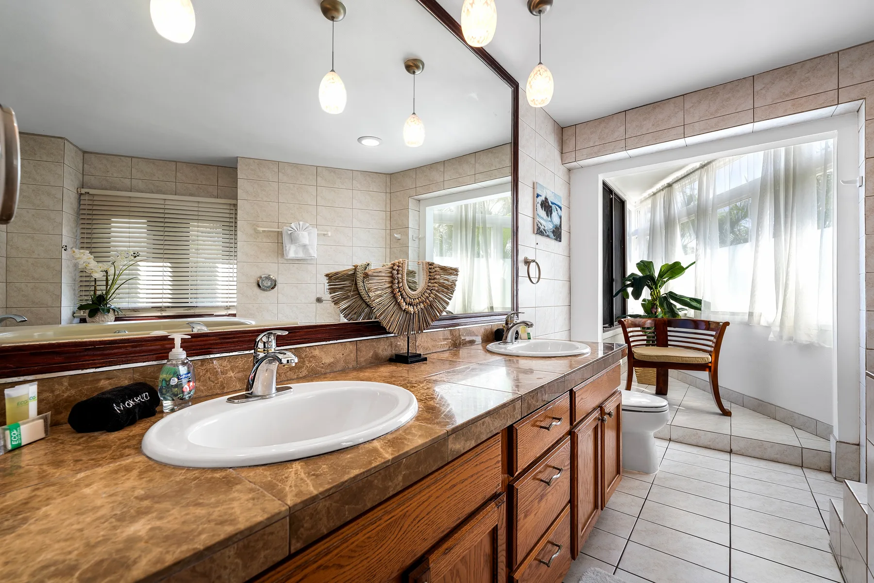 Un baño luminoso con azulejos, una encimera larga y dos lavabos.