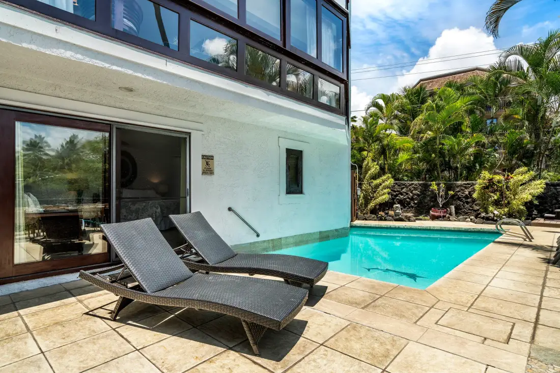 Una piscina junto a un edificio moderno, con asientos de descanso en la terraza de baldosas.