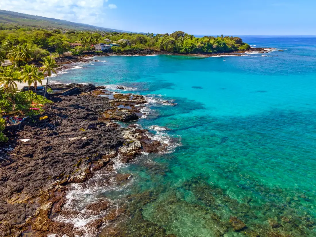 Una costa tropical con aguas turquesas claras, orilla rocosa y vegetación verde.