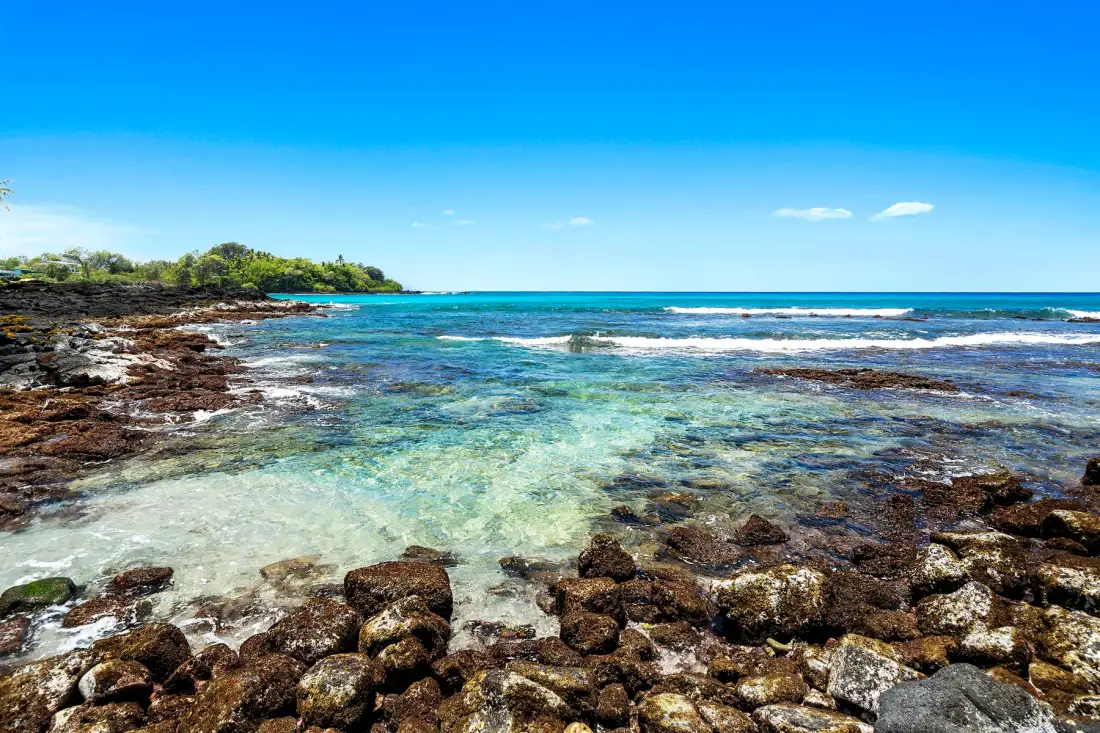 Una costa rocosa bordea aguas claras y poco profundas bajo un cielo azul.