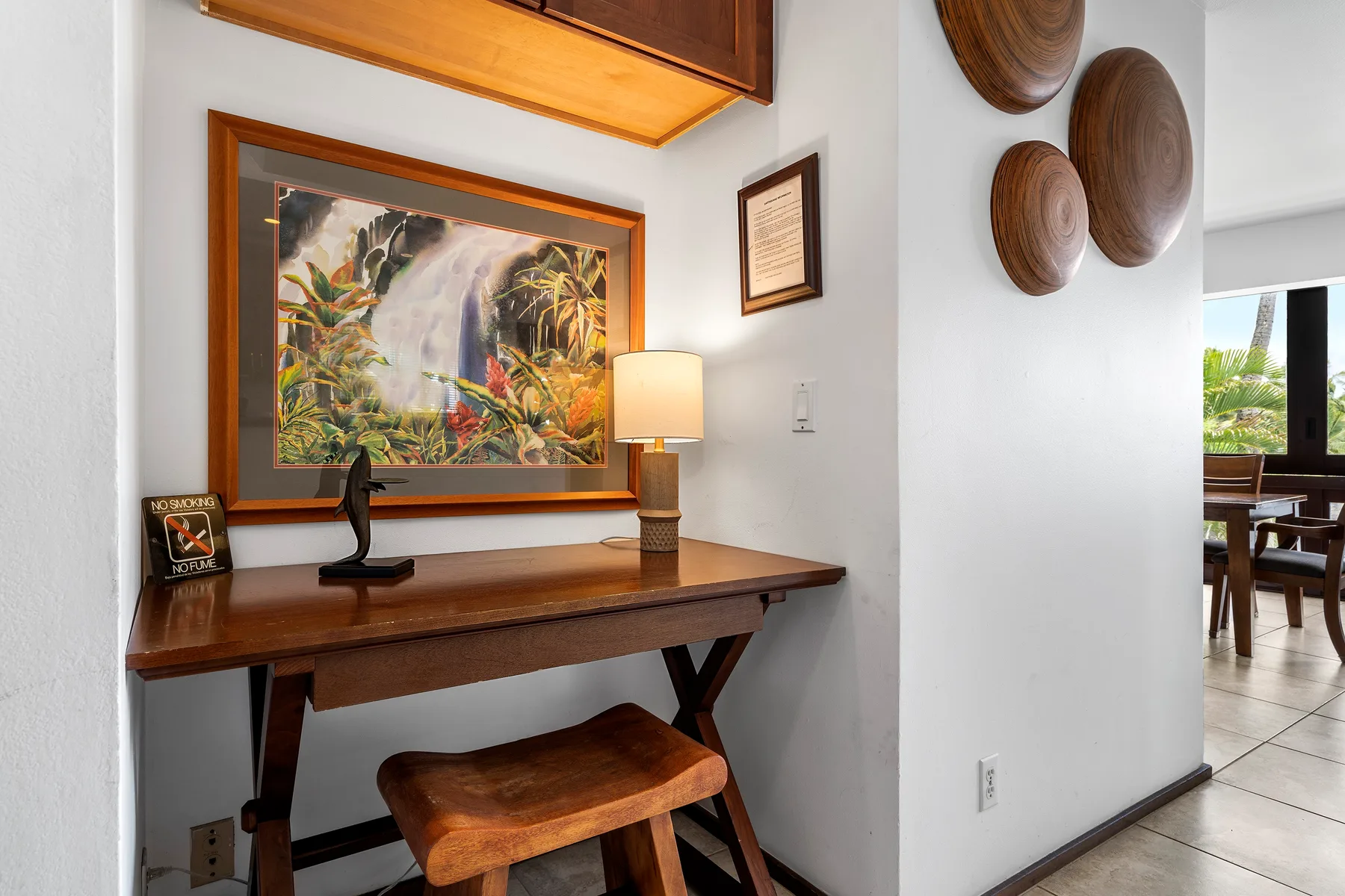Un escritorio de madera está bajo una pintura enmarcada de un paisaje tropical.