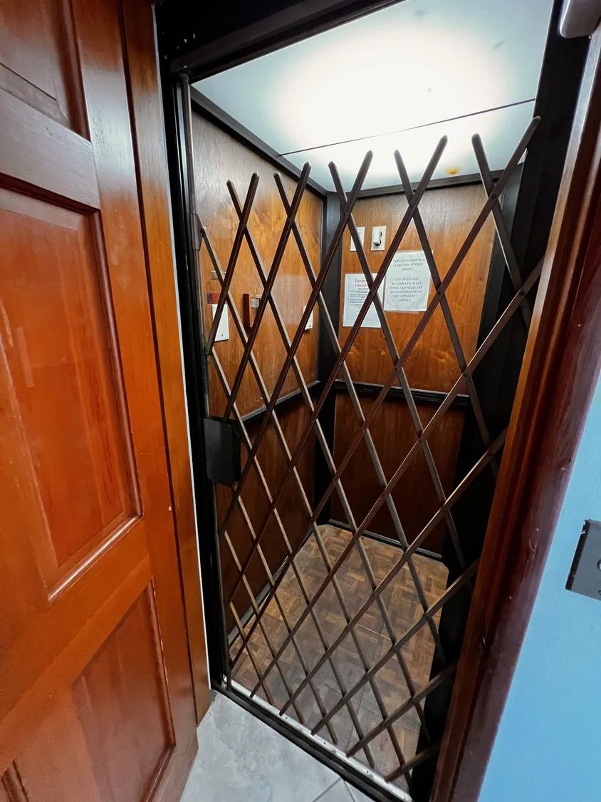 Un ascensor con una reja metálica plegable y paredes revestidas de madera.