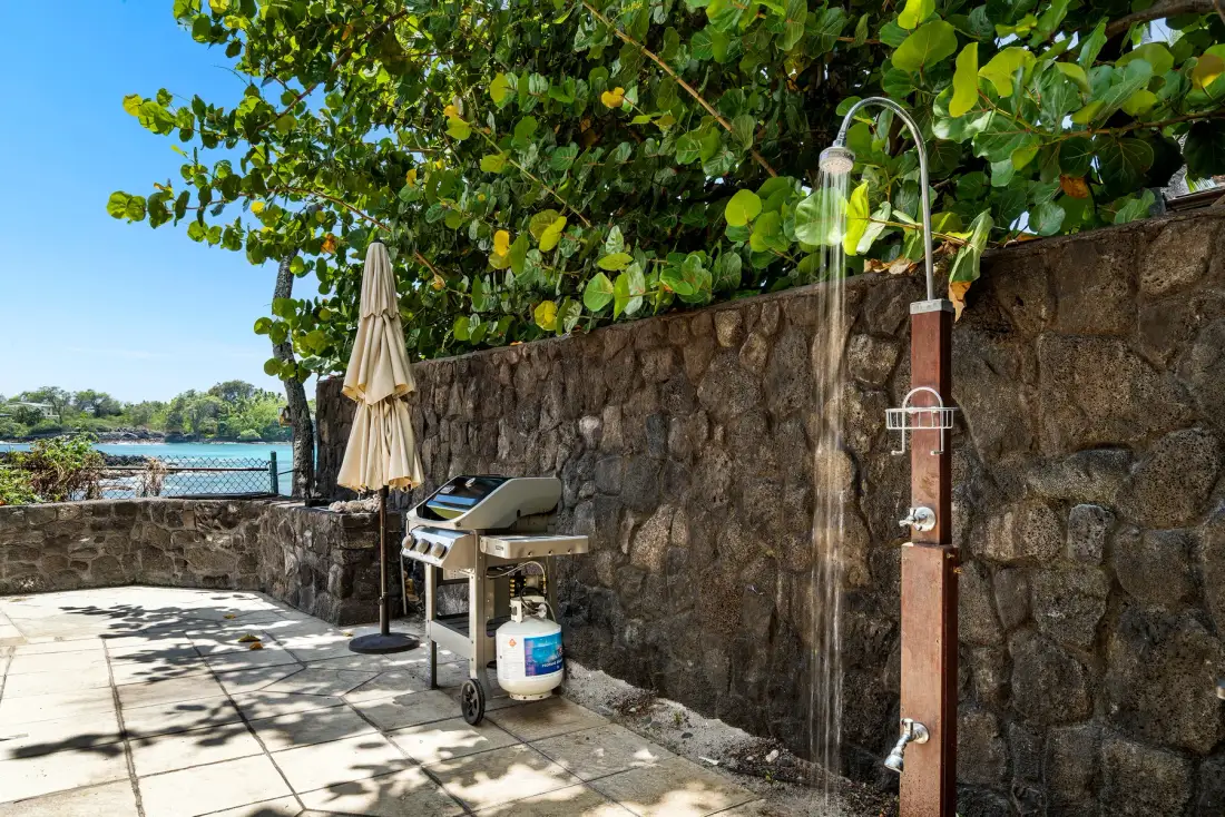 Un patio al aire libre con una parrilla y una ducha junto a un muro de piedra.