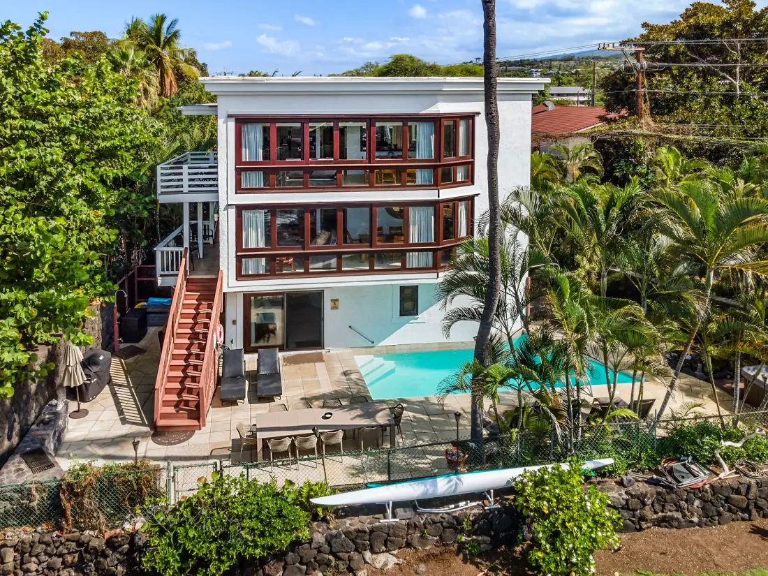 Una casa moderna de varios pisos da a una piscina rodeada de vegetación tropical.