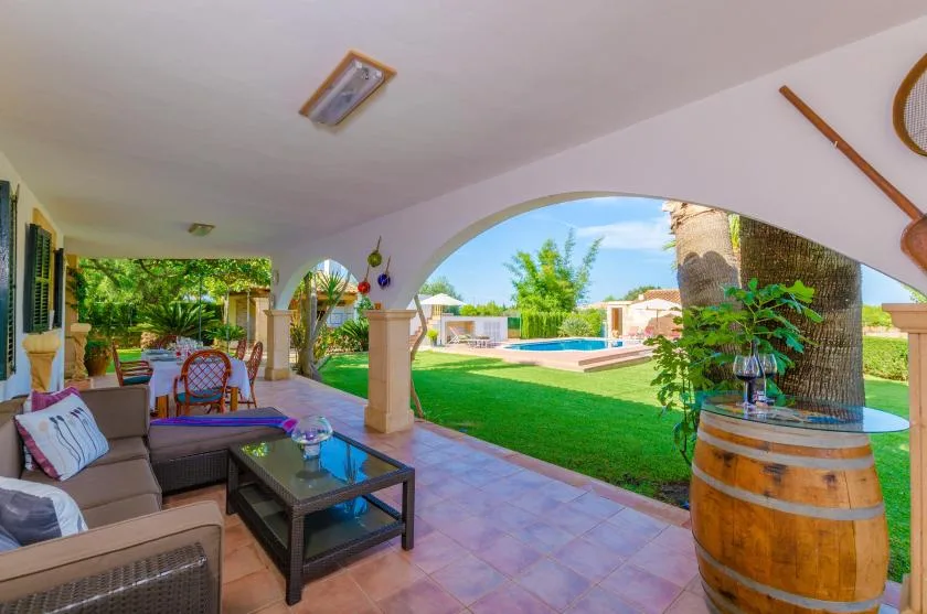 Un patio cubierto con asientos da a un jardín y una piscina.