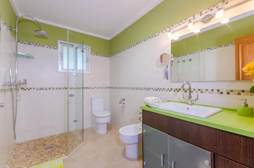 Un baño con ducha de cristal, inodoro y lavabo con mueble verde.