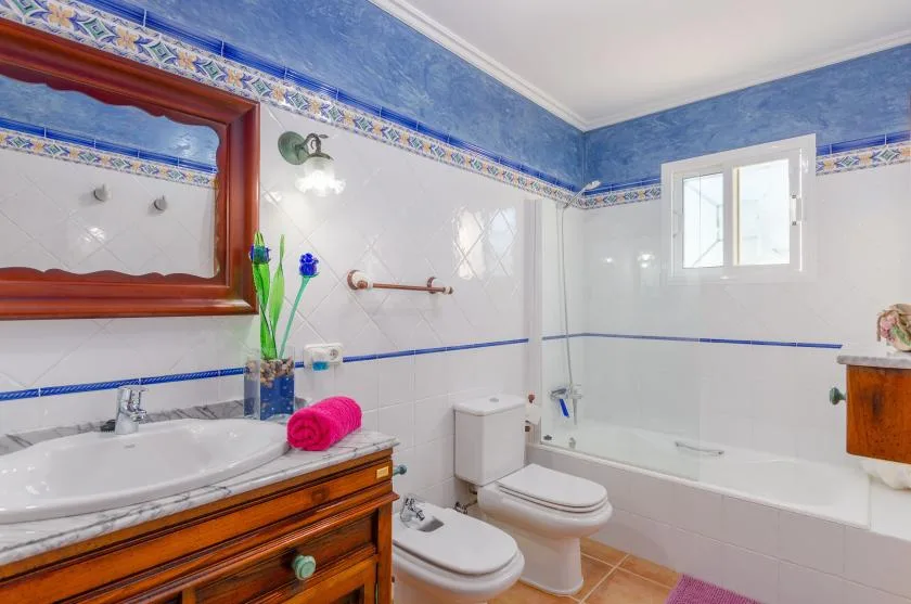 Un baño con lavabo, inodoro y bañera bajo una ventana.