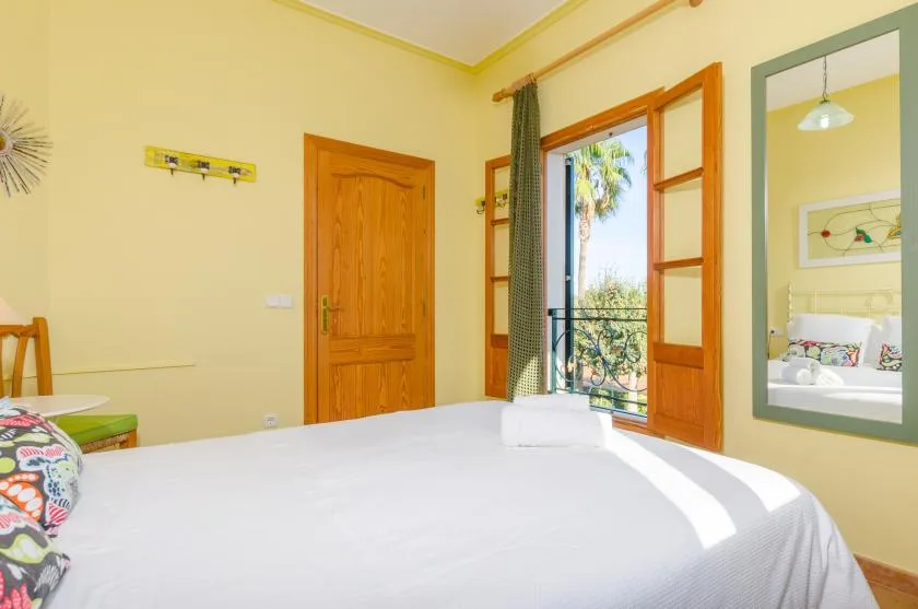 Un dormitorio luminoso con una cama tendida y puertas abiertas al balcón.