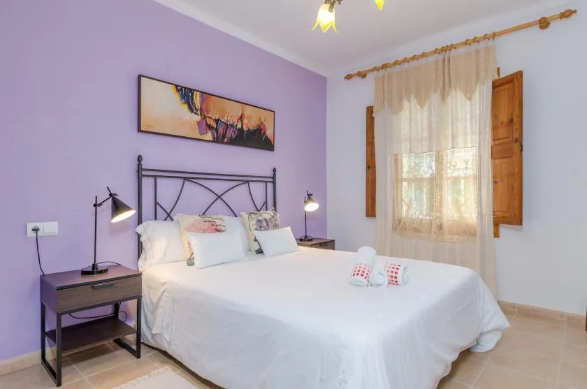 Un dormitorio con una cama bajo un cuadro enmarcado y una ventana con cortinas.