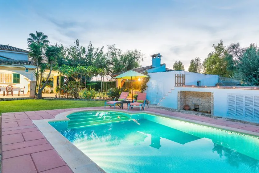 Zona de piscina al aire libre con asientos y jardín al anochecer.
