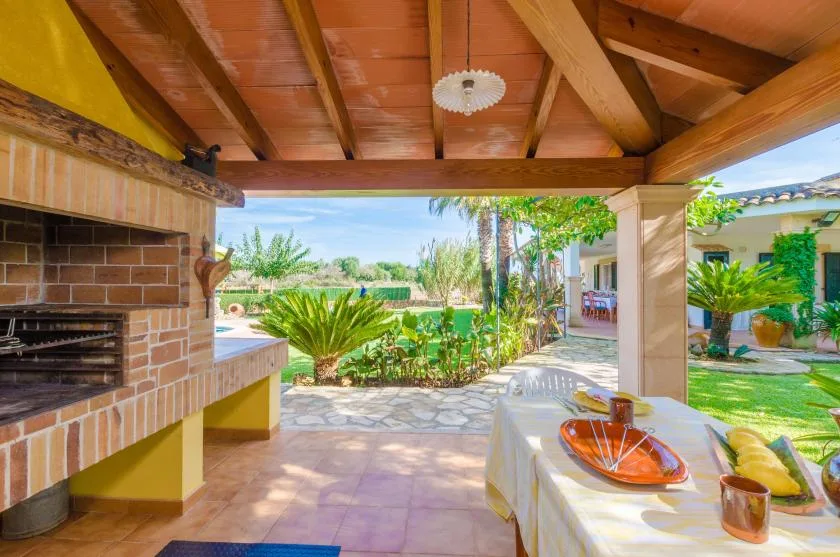 Un patio cubierto con barbacoa de ladrillo da a un jardín y una piscina.