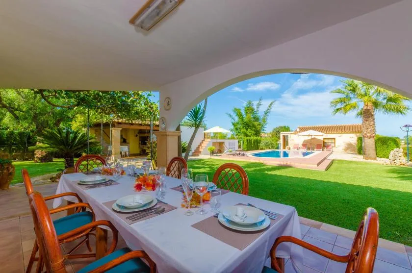 Una zona de comedor exterior cubierta da a un césped y una piscina.
