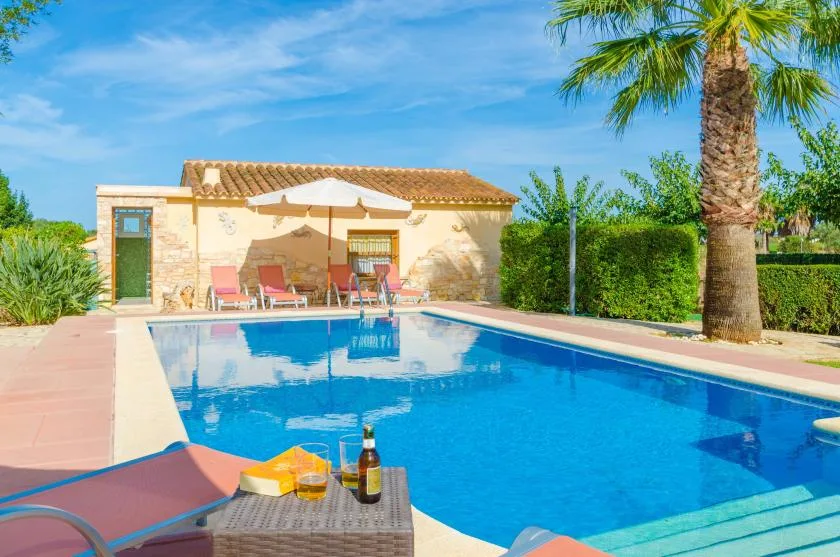 Una piscina al aire libre junto a un patio soleado con asientos y una sombrilla.