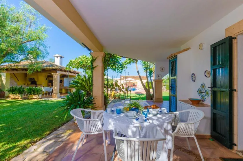 Un patio cubierto tiene una mesa de comedor al aire libre con vistas a un jardín verde.
