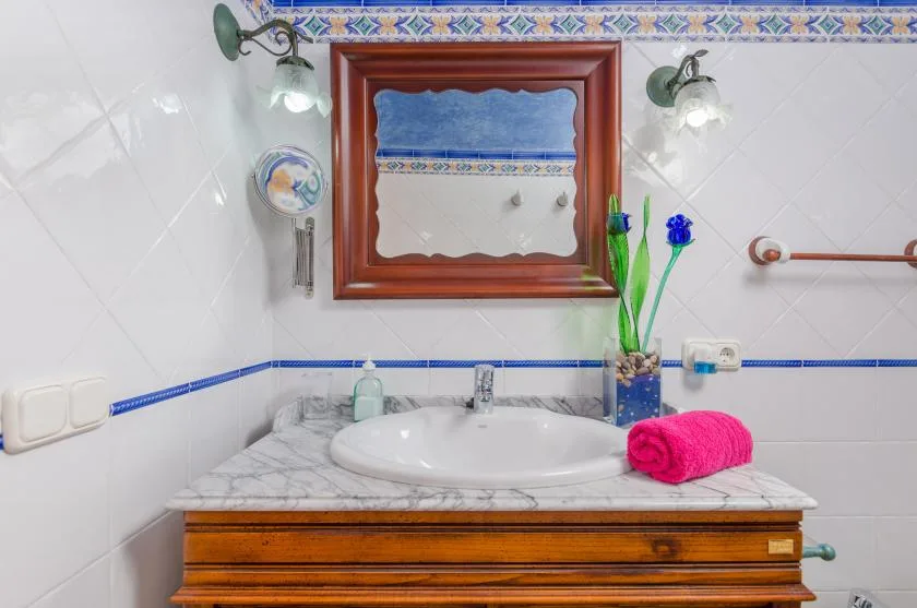 Un lavabo de baño con azulejos, un fregadero blanco y cajones de madera.