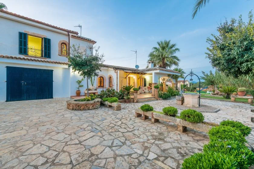 Una casa blanca da a un patio empedrado con parterres y palmeras.