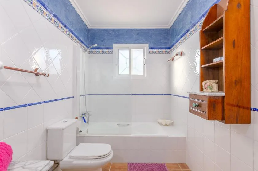 Un baño con azulejos, bañera, inodoro y estantería de madera en la pared.