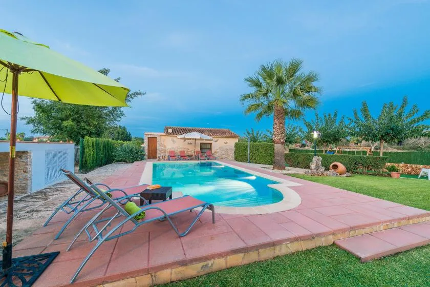 Una piscina al aire libre está rodeada por un patio pavimentado, asientos reclinables y vegetación.