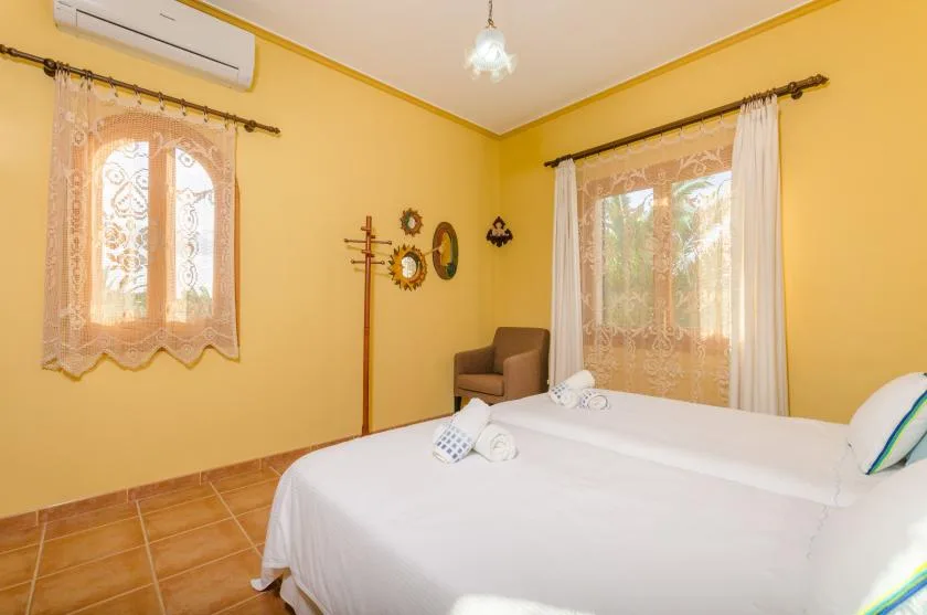 Un dormitorio con ropa de cama blanca, ventanas con cortinas y una silla pequeña.