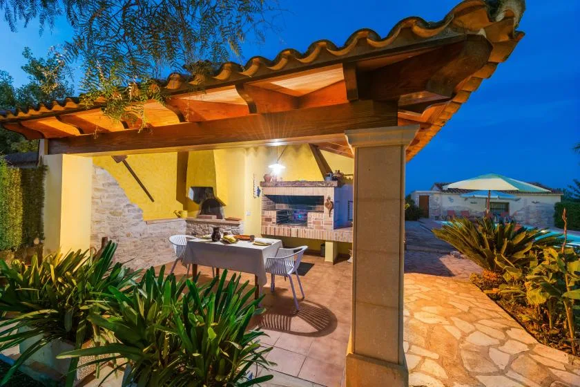 Comedor al aire libre bajo un patio cubierto, con una barbacoa integrada.
