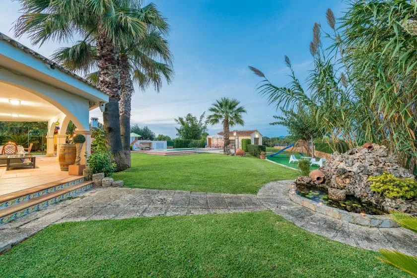 Un jardín cuidado con césped, palmeras y una piscina.