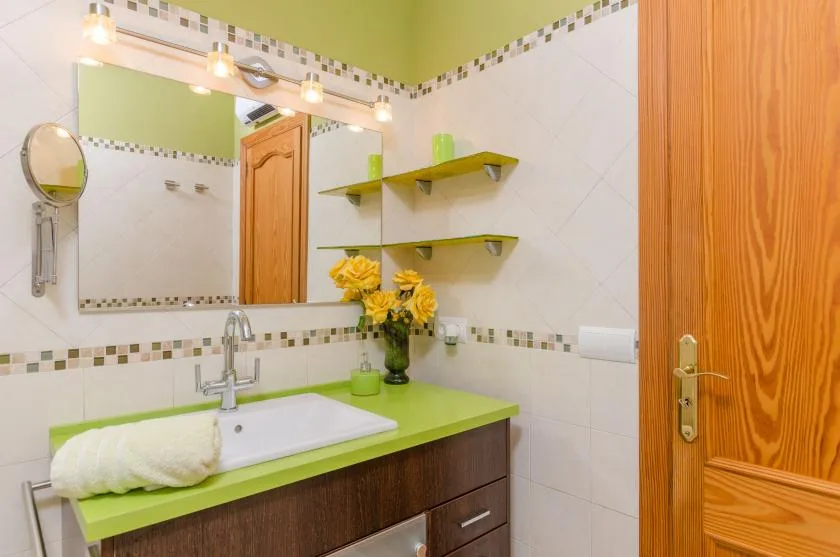 Un tocador de baño con lavabo, espejo y encimera verde.