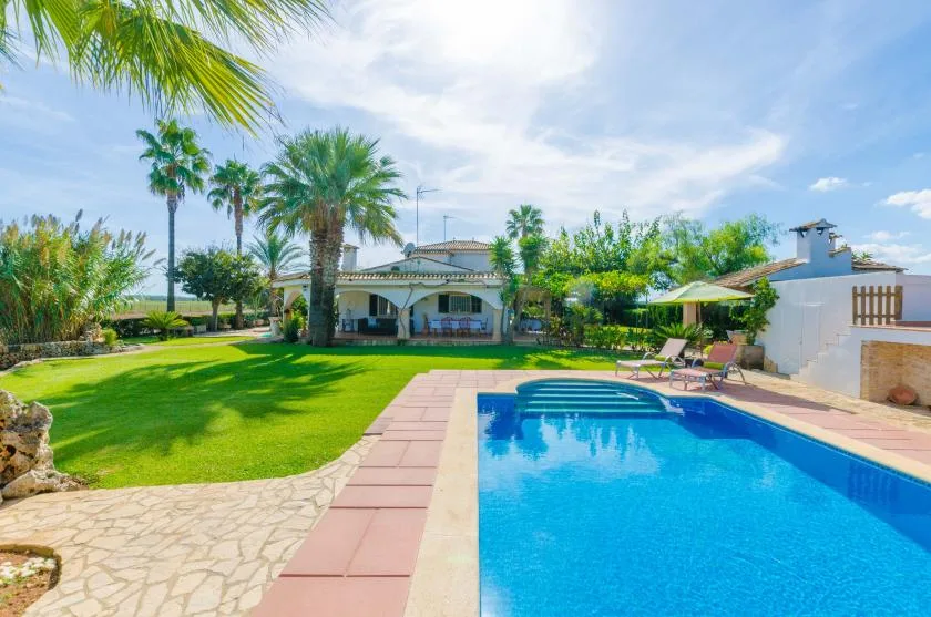 Una piscina junto a un césped verde y una casa baja bajo un cielo despejado.