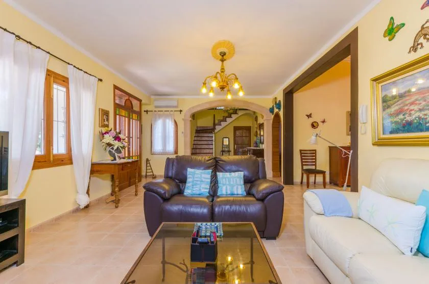 Una sala de estar con asientos alrededor de una mesa de centro de vidrio y una escalera al fondo.