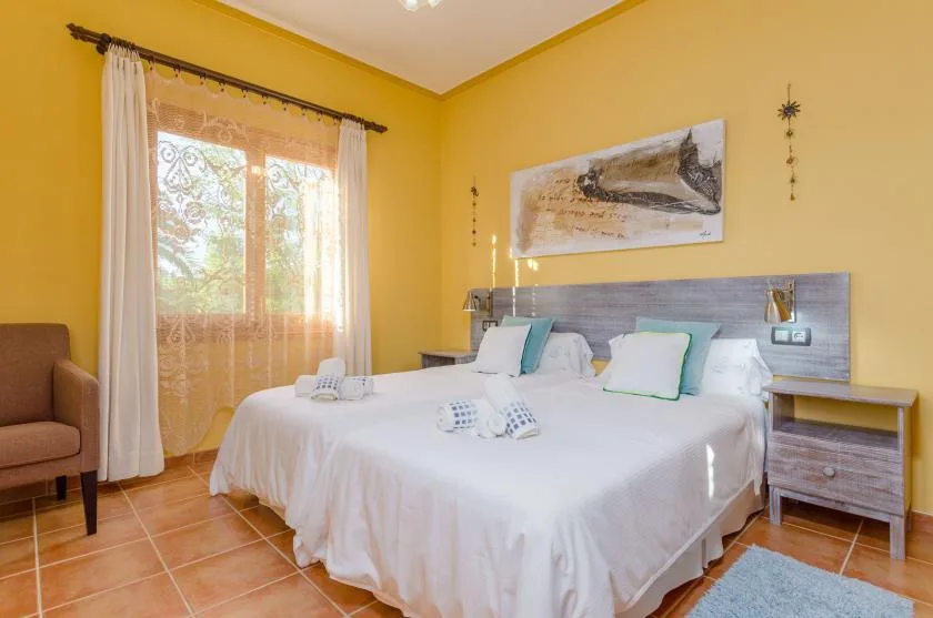 Un dormitorio con una cama grande, ropa de cama blanca y una ventana iluminada por el sol.