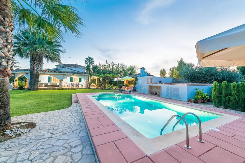 Una piscina al aire libre está junto a un patio pavimentado y un jardín.