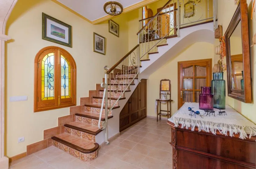 Una escalera interior asciende junto a una ventana arqueada de vidrio emplomado.