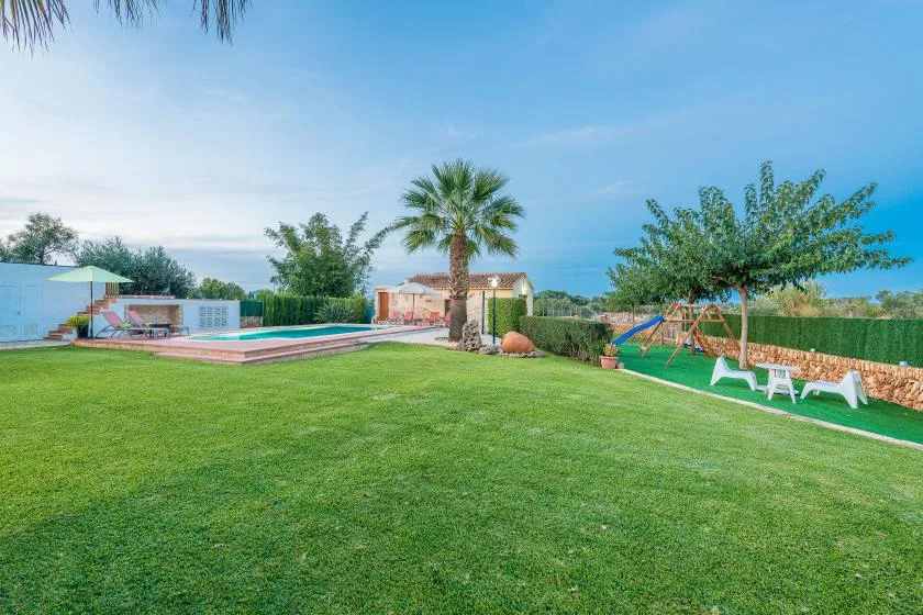 Un jardín ajardinado con césped, piscina, palmera y asientos al aire libre.